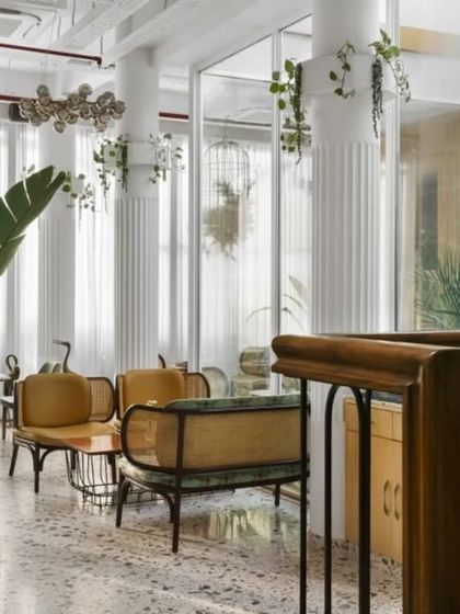 This view showcases the interplay of textures, from the polished terrazzo floor to the fluted white columns and warm wood furniture. Hanging plants and large potted greenery are placed throughout to ensure nature is felt in every corner.