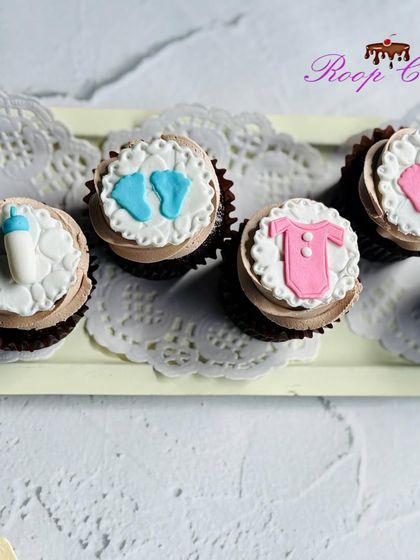 Classic baby shower cupcakes featuring handmade fondant toppers. This set includes adorable baby footprints, a milk bottle, and a little onesie, perfect for celebrating the upcoming arrival.