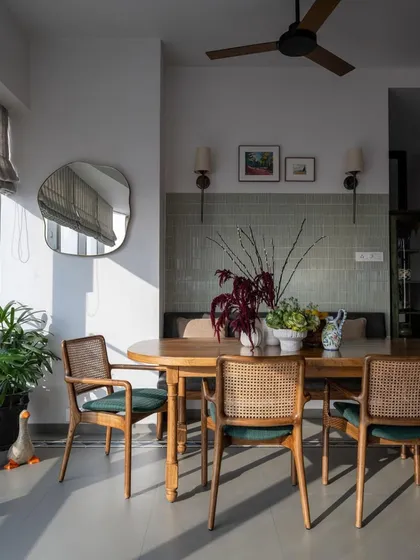 Sunlight streams into this serene dining area from the 'Inde Blue' project. The space is simple and calming, with classic cane-back chairs, a smooth wooden table, and an organic-shaped mirror that reflects the light beautifully.