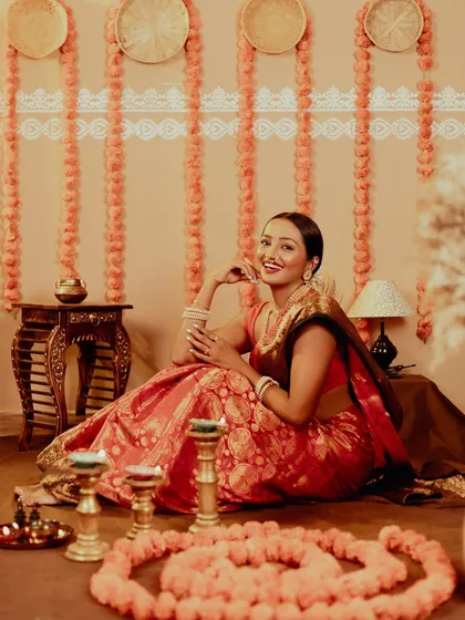 A wide shot that captures the whole festive atmosphere. The model is seated amidst a rangoli of flowers, creating a beautiful, traditional scene.
