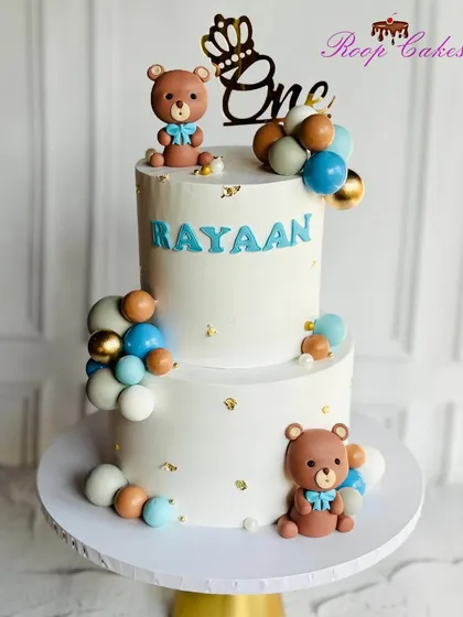 Snuggles, giggles, and one sweet year. This custom two-tier cake for a baby's first birthday features cute teddy bears and a cascade of balloons.
