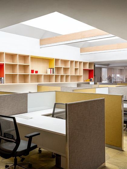 This workstation area at the Stainless Steel Office features a large skylight and integrated shelving. The cubicle partitions in muted tones of grey and yellow create a defined yet collaborative workspace for the design studio.