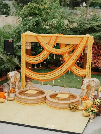 This traditional Haldi setup features a backdrop of draped marigold garlands and elephant statues for a touch of regal charm. The custom seating urns are filled with flowers, making the couple the center of this beautiful ceremony.