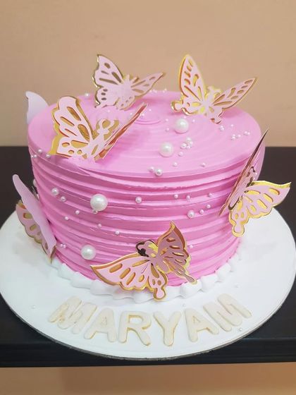A lovely pink butterfly cake with textured frosting and gold-accented butterflies, personalized with the name "Maryam."