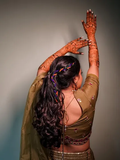 A graceful pose from behind, highlighting the bride's beautiful hairstyle and her arms raised to display her stunning mehndi design.