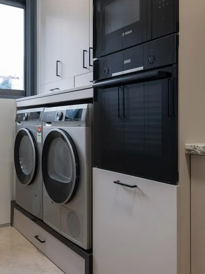 Here, the washer and dryer are placed next to the oven tower. This layout consolidates all the home's "workhorse" appliances into one zone, creating an efficient and practical workflow.