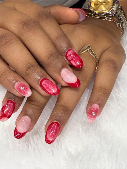 A beautiful red marble or "bloom" effect nail art. This design features a sheer base with abstract watercolor-like red patterns, accented with tiny rhinestones.