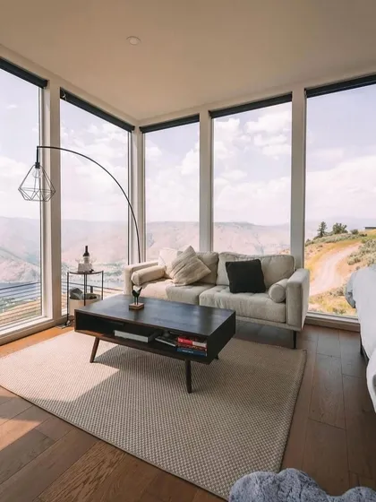 The living area of this mountain cabin features floor-to-ceiling windows that frame the stunning landscape. The minimalist furniture and natural materials create a sense of calm and connection to the outdoors.