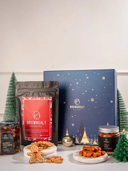 This Christmas hamper balances sweet, savory, and festive. It features our Xmas Special Granola, a honey-infused jar, spicy chili cashews, and gingerbread cookies, offering a delightful variety for any recipient.