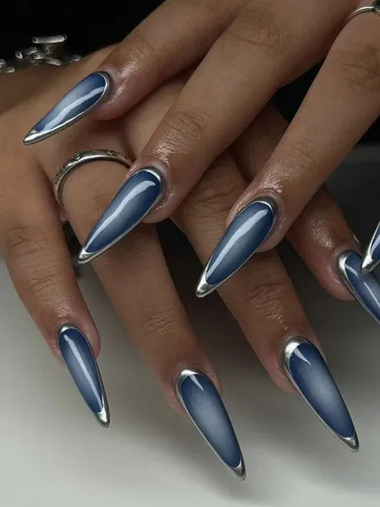 A sleek and modern design featuring long, sharp stiletto nails with a denim-blue cat eye effect. The look is framed with a silver chrome edge for an extra touch of metallic detail.