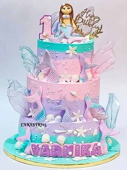 A magnificent three-tier mermaid-themed cake. This 5kg fruit-flavored creation features a mermaid topper, fondant fishtails, and beautiful aqua, lavender, and pink coloring.