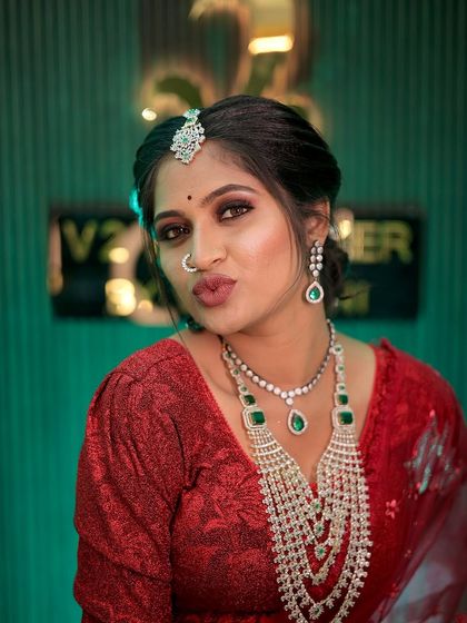 A playful and confident shot of the bride in her red reception outfit. The puff-sleeve blouse adds a touch of modern trendiness, while the magnificent layered diamond necklace ensures the look remains timelessly elegant.