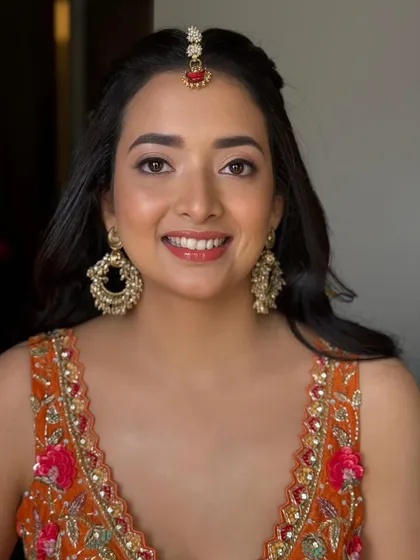 A close-up of Shreya's radiant Haldi look. The makeup is fresh and glowing, with a glossy lip and soft eyes that complement her bright orange lehenga.