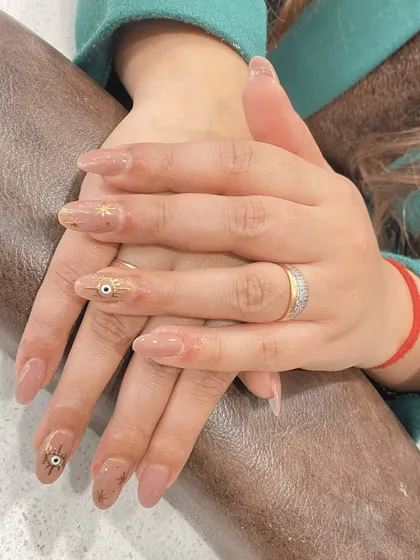 This trendy design features the popular evil eye symbol for a touch of mystique. I painted the delicate symbols and tiny gold stars over a sheer nude base on these elegant almond-shaped extensions.