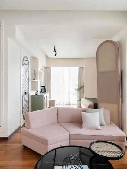 A soft pink L-shaped sofa adds a playful touch to this living area, balanced by a modern floor lamp and a cane screen partition that adds texture and warmth.