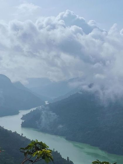 A river winding its way through a deep valley, with clouds hanging low over the mountains. A truly dramatic and beautiful scene.