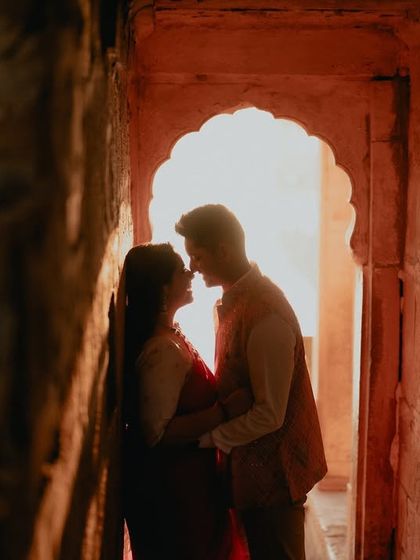 A silhouette of a couple sharing an intimate moment within a stone archway in Jaisalmer. The warm, glowing light creates a romantic and mysterious atmosphere, perfect for a heritage pre-wedding shoot.