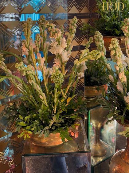 A close-up of fresh tuberose flowers in a brass vase on a mirrored stand, reflecting the intricate patterns of the venue's decor.
