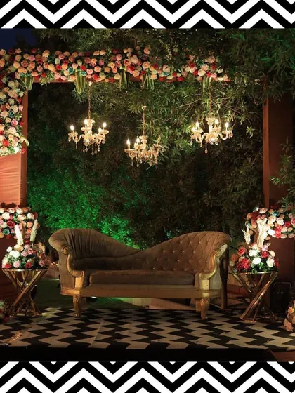 The couple's seating area for the Sangeet, featuring a vintage-style sofa, floral arrangements, and elegant chandeliers, all set against the modern dance floor.