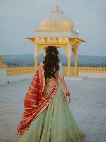A beautiful back-shot of the bride in her pastel lehenga, walking on a palace rooftop during her Mehendi photoshoot.