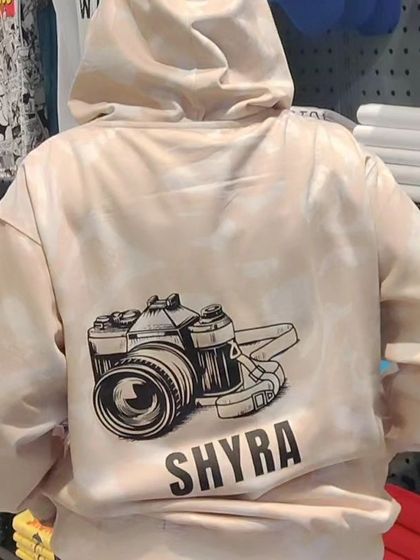 A close-up of a custom hoodie with a camera graphic and the name "Shyra" printed on the back. A perfect example of personalization.