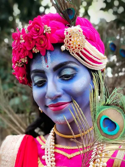 A close-up of the Krishna makeup, featuring a vibrant blue base, intricate white detailing, and a beautiful headpiece adorned with flowers and a peacock feather.