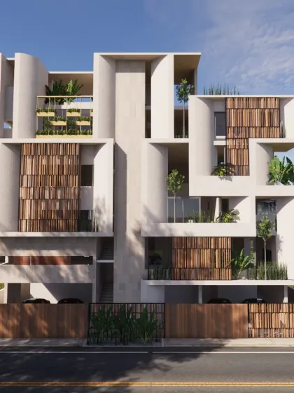 The facade of a multi-family residence in Gulbarga, designed as two stacked duplex units for a joint family. The structure features interlocking geometric forms, recessed balconies with plants, and wooden screens that provide both privacy and effective sun shading in a modern architectural style.