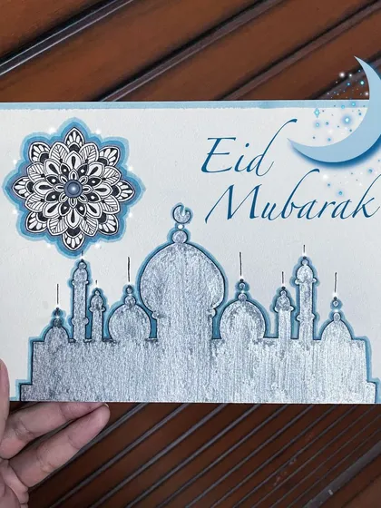 An Eid Mubarak greeting card I designed, featuring a silver silhouette of a mosque and a detailed blue and black mandala. The silver paint gives the piece a festive, metallic shine.