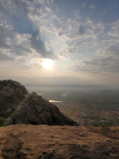 The sun breaking through the clouds, casting a golden light over the vast plains visible from the top of the hill.