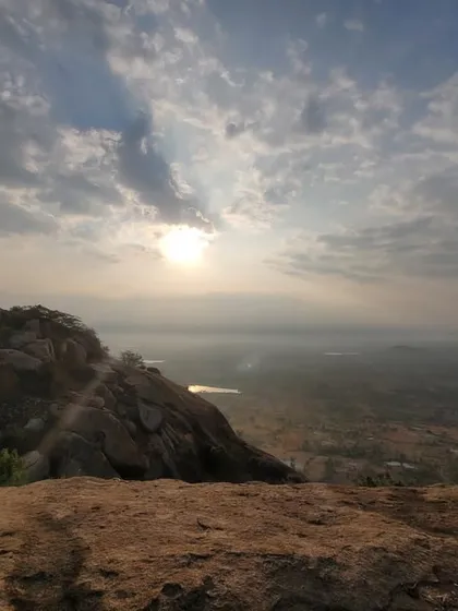 The sun breaking through the clouds, casting a golden light over the vast plains visible from the top of the hill.