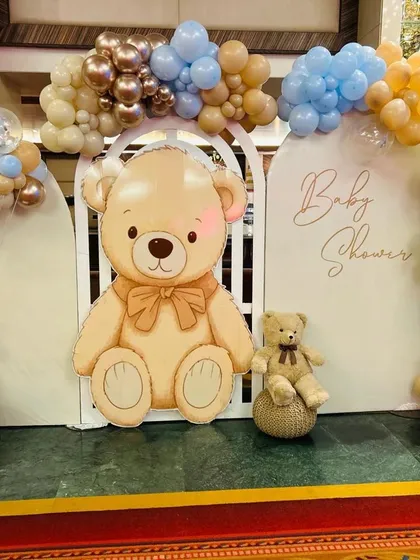 A cute and cuddly teddy bear themed baby shower. The large teddy bear cutout serves as the main attraction, framed by arches and a beautiful balloon garland in soft, welcoming colors.