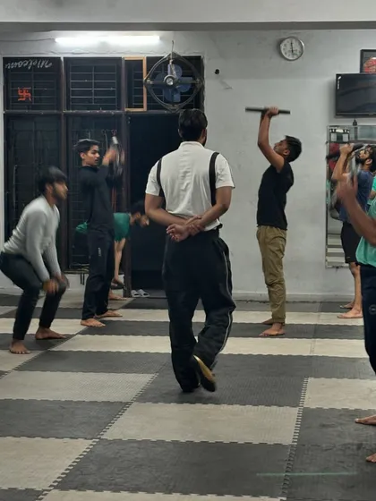 A look at our group strength training from behind. Students are engaged in various exercises, including overhead presses with bars, demonstrating the diversity of our workout programming.