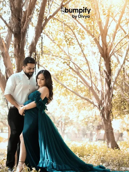 A beautiful couple's portrait taken in a sunlit grove. The dad-to-be holds his partner close as her stunning teal gown trails behind her, creating a truly cinematic pregnancy photo.