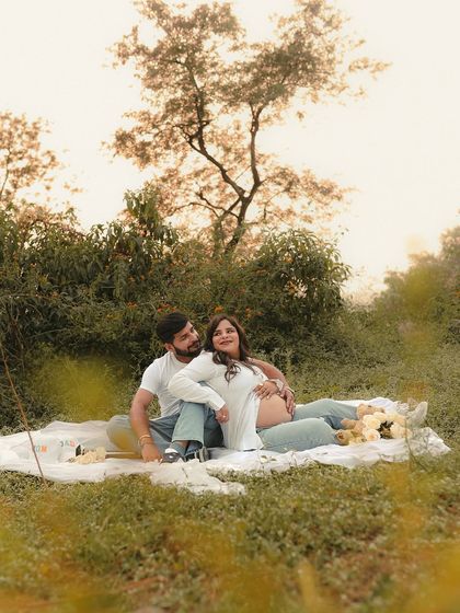 A romantic outdoor picnic scene. The couple relaxes on a blanket in a grassy field, the soft, warm light creating a dreamy and intimate atmosphere.