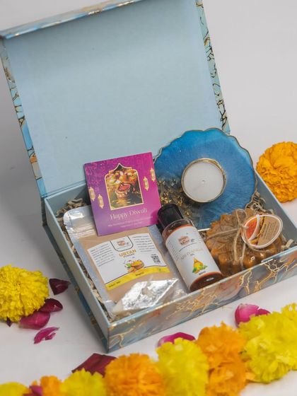 A modern and elegant Diwali hamper featuring Ubtan powder, Abhyanga oil, and handmade soap, complemented by a beautiful blue resin art candle holder.