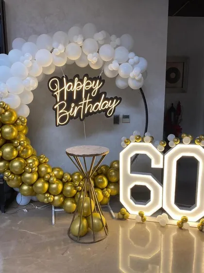 An elegant and classic 60th birthday celebration setup. We used a sophisticated gold and white color scheme with a large balloon ring, a modern neon 'Happy Birthday' sign, and prominent light-up marquee numbers to mark the special milestone.
