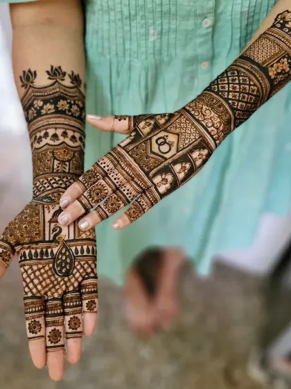 A stylish engagement mehendi with a peacock on one palm and interlocking rings on the other. The design is modern, with a lotus armlet and geometric patterns.