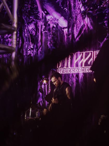 An atmospheric shot of a guitarist performing at Jazz Weekender, with the neon logo glowing behind them. The lighting and stage design are crucial elements I manage to create a memorable experience.