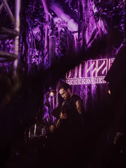 An atmospheric shot of a guitarist performing at Jazz Weekender, with the neon logo glowing behind them. The lighting and stage design are crucial elements I manage to create a memorable experience.