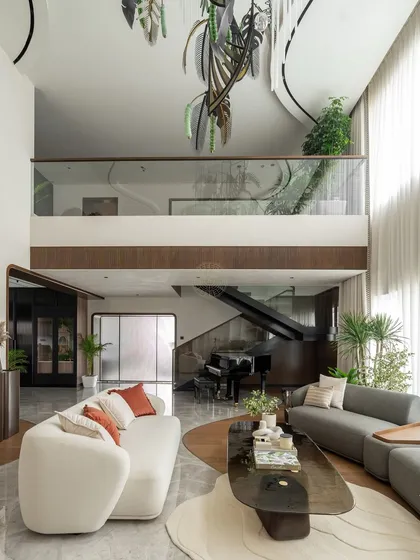 This angle showcases the open and connected layout of the Kolkata home. The living area flows seamlessly towards the den and the upper floor, with curved architectural lines in the mezzanine railing and flooring that guide the eye through the space.