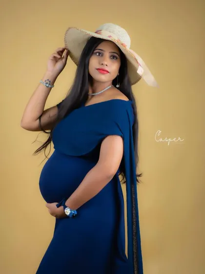 A stylish and chic portrait. The mom-to-be wears a simple blue dress and a wide-brimmed hat, creating a fashionable and modern maternity look.