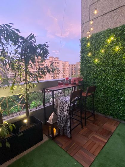 We created this charming bar nook on a small balcony using interlocking wood deck tiles and a patch of artificial grass. The setup is perfect for enjoying the evening, with a vertical garden and string lights adding to the warm, inviting atmosphere.
