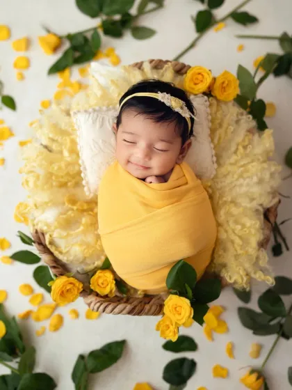 That sleepy little smile is just everything. A perfectly swaddled newborn girl in a yellow wrap, dreaming among the rose petals.