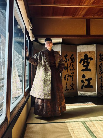 Inside a traditional Japanese house, wearing a brocade coat that complements the beautiful calligraphy screens.