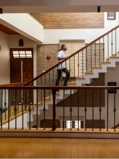 A person ascends the staircase, illustrating the human scale and movement within the multi-level design. The exposed brick wall provides a continuous textured backdrop.