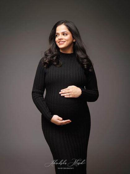 A classic three-quarter portrait in a simple black dress, capturing a warm smile and the gentle embrace of the baby bump.