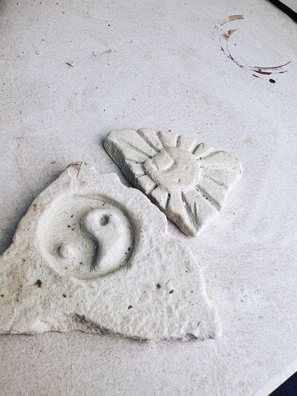 Small carved pieces showing a yin-yang symbol and a sun, made by participants experimenting with different designs.