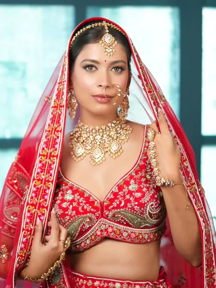 A traditional bridal pose with the dupatta veil, highlighting the intricate choker, earrings, and nath. This is a classic shot that every bride cherishes.