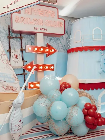 A detailed shot of the party entrance, with a large 'River's Sailor Club' sign, light-up arrows, and a cascade of balloons.