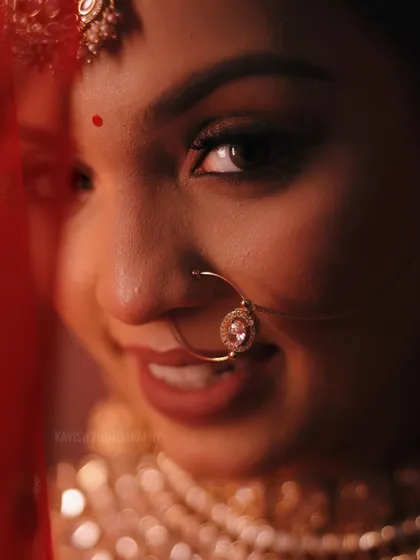 A playful and intimate bridal portrait taken through her red veil. The focus is on her joyful expression and the details of her nose ring.